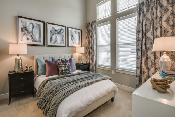 Bedroom with carpet, plush bed with headboard, bedside tables with lamps, framed art, and large windows.