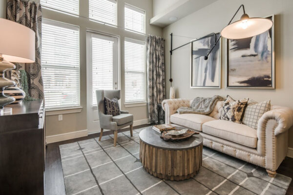 Living room with pattern rug, plush couch, framed artwork, large lamp, and large windows.