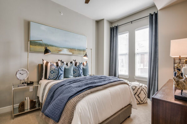 Bedroom with carpet, plush bed with headboard, bedside tables with lamps, and large window.