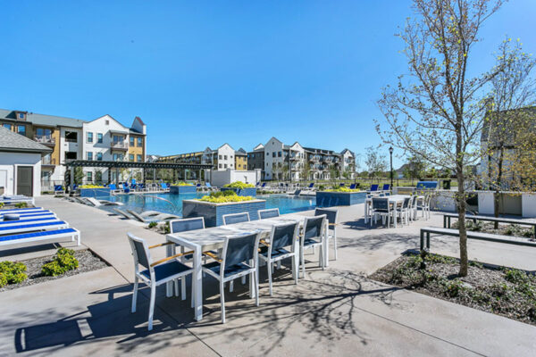 Pool area with lounge chairs, dining tables, and lush landscaping.