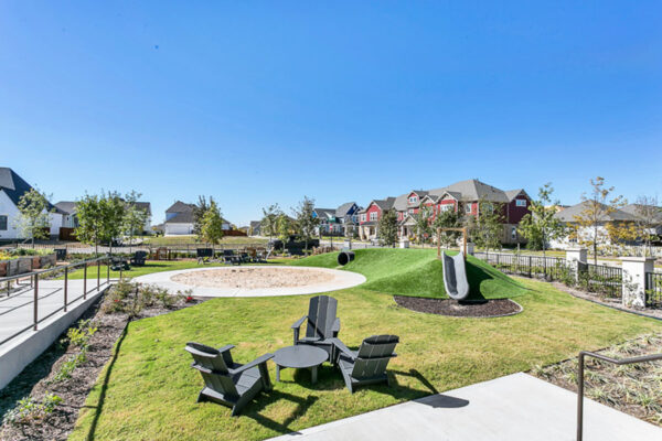 Playground with lounge chairs, grassy hills with slides and play equipment, and lush landscaping.