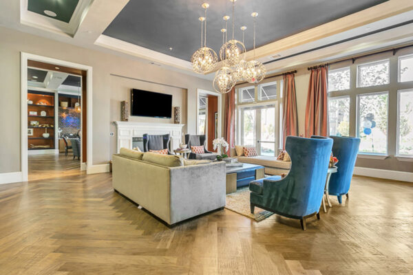 Lounge with herringbone floor, plush seating, fireplace with TV, and large bright windows.