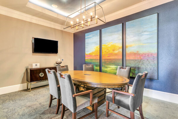 Lounge with plush carpet, elegant table with chairs, TV, and large triptych artwork.
