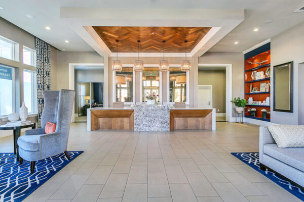 Clubroom with tile floor, elegant leasing desk with light fixtures, and shelves with decor.