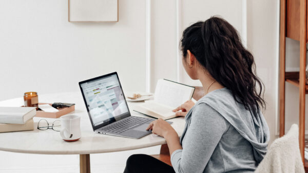 Person working on laptop at table with notebook, coffee cup, and candle.